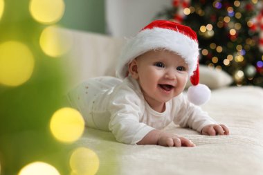 Noel Baba şapkalı şirin bir bebek Noel ışıklarına karşı kanepede, bokeh etkisi