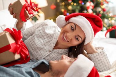 Pijamalı ve Noel şapkalı mutlu çift evde yatağında hediyeler bekliyor.