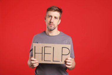 Mutsuz adam kırmızı arka planda kelime yazılı karton tabela tutuyor.