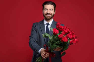 Sevgililer Günü. Kırmızı arka planda gül buketi olan yakışıklı adam.
