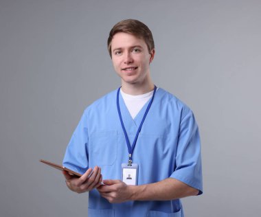 Gri arkaplanda tableti olan bir tıp asistanı portresi