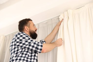 Evde pencere perdelerini asan adam, düşük açılı görüntü.