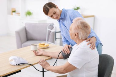 Bakıcı evde yaşlı kadının kan basıncını ölçüyor.