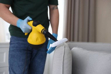 Haşere kontrol işçisi kanepeyi temizliyor. Kapalı alanda buhar temizleyicisi var.