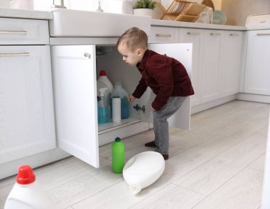 Evde çocuk güvenliği. Küçük çocuk mutfakta temizlik ürünleriyle oynuyor.