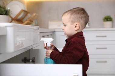 Evde çocuk güvenliği. Mutfakta bir şişe temizlik malzemesi olan küçük bir çocuk.