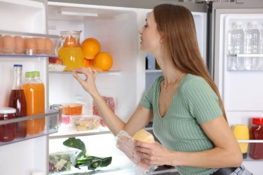 Jambonlu ve peynirli kadın mutfaktaki açık buzdolabının yanında.