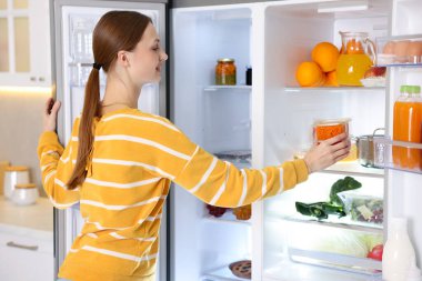 Kadın mutfaktaki buzdolabının rafına yiyecek koyuyor.