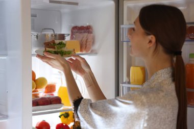 Kadın sandviçleri buzdolabından dışarı çıkarıyor.