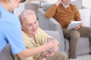 Huzurevindeki yaşlı kadına bir bardak su veren bakım görevlisi, yakın plan.