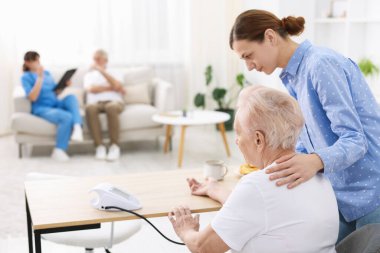 Bakıcı evde yaşlı kadının kan basıncını ölçüyor.