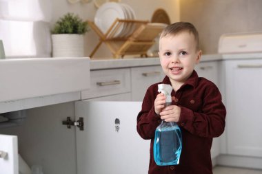 Evde çocuk güvenliği. Mutfakta bir şişe temizlik malzemesi olan küçük çocuk, mesaj için yer var.