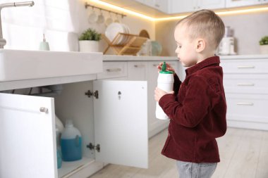 Evde çocuk güvenliği. Mutfakta bir şişe temizlik malzemesi olan küçük bir çocuk.