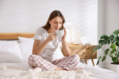 Beautiful woman with cup of aromatic coffee on bed at home. Space for text