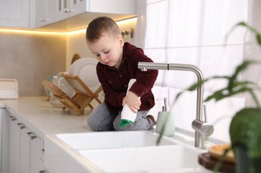 Evde çocuk güvenliği. Küçük çocuk mutfakta lavabonun yanında tozla oynuyor.