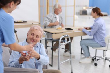 Huzurevindeki yaşlı kadına bir bardak su veren bakım görevlisi, yakın plan.