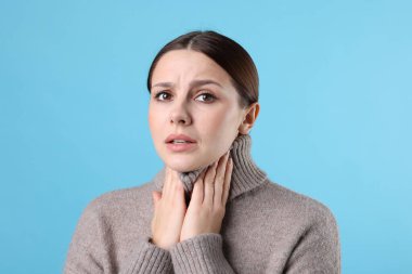 Açık mavi arka planda boğaz ağrısı çeken bir kadın. Soğuk Semptom