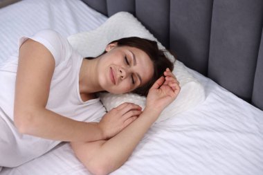 Ortopedik yastıkla yatakta uyuyan genç bir kadın. Sağlıklı duruş