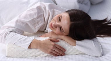 Ortopedik yastıkla yatakta uyuyan genç bir kadın. Sağlıklı duruş