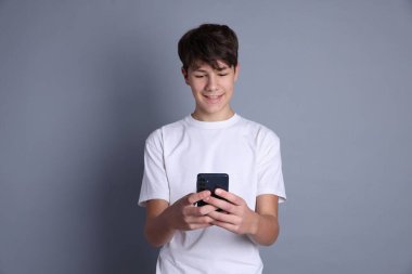 Genç çocuk gri arka planda akıllı telefon kullanıyor.