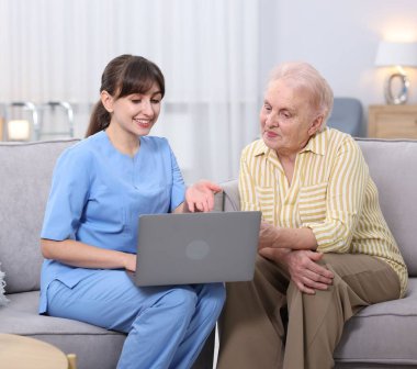 Huzurevinde yaşlı bir kadına dizüstü bilgisayar kullanmayı öğreten bakım işçisi.