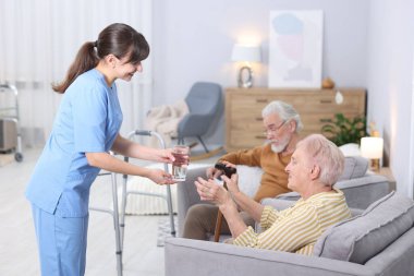 Huzurevindeki yaşlı kadına bir bardak su veren bakıcı.