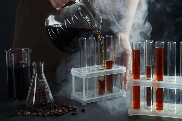 Siyah masada cam test tüpüne damlatan kadın, yakın plan.