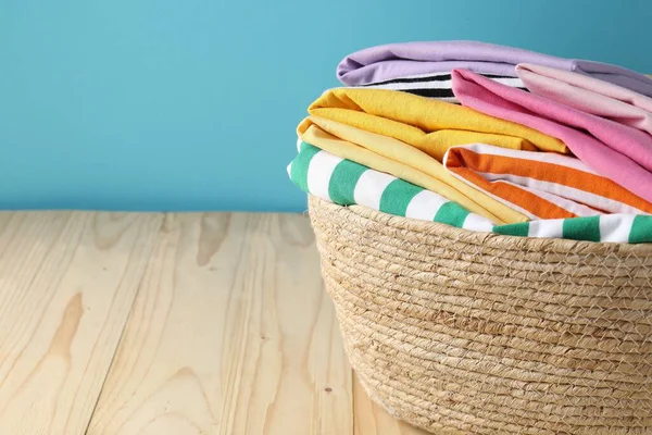 Açık mavi duvarın yanındaki ahşap masada giysileri olan çamaşır sepeti, yakın plan. Metin için boşluk