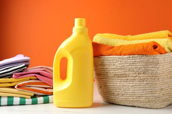 Çamaşır sepetinde havlular, giysiler ve bir şişe deterjan turuncu duvarın yanında, kapalı.