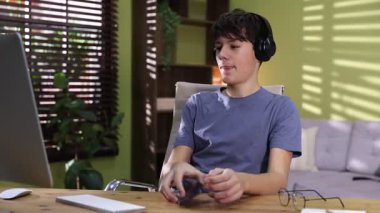 Kulaklıklı, akıllı telefonlu, ahşap masada müzik dinleyen genç bir çocuk.