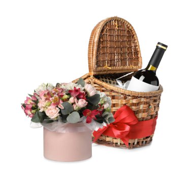 Hasır sepetin içinde bir şişe şarap ve beyaz üzerine izole edilmiş bir buket güzel çiçek.