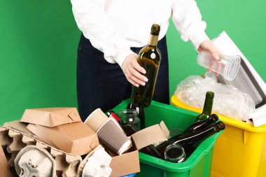 Yeşil arka planda çöp kutusuna çöp atan kadın, yakın plan. Atık sıralama