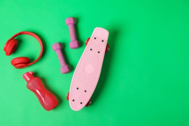 Tahta, su şişesi, halterler ve kulaklıklar yeşil arka planda, düz konum. Metin için boşluk