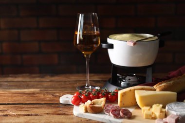 Lezzetli eritilmiş peynirli fondü, abur cuburlar ve ahşap masada şarap. Metin için boşluk