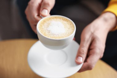 İçerideki ahşap masada bir fincan aromatik kahveli adam, yakın plan.