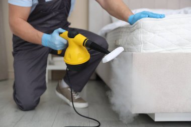 Haşere kontrol işçisi yatağı temizliyor, kapalı alanda buhar temizleyicisiyle, yakın plan