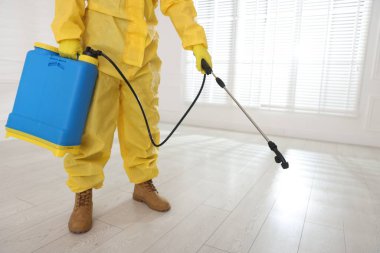 Koruyucu kıyafetli haşereci böcek ilacı sıkıyor, yakın plan.