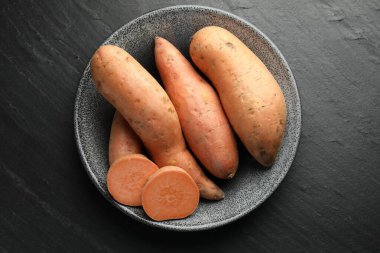 Tam ve tatlı patatesleri kasede, koyu dokulu masada, üst tarafta.