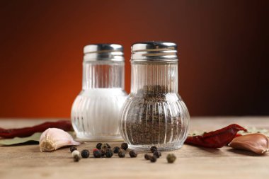 Ahşap masada baharatlı tuzluk ve biberlikler koyu turuncu arka planda, yakın planda.
