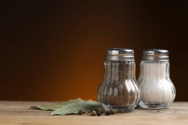 Ahşap masada baharatlı tuzluk ve biber karıştırıcıları kahverengi gradyan arka planda, yakın plan. Metin için boşluk