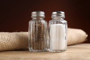 Ahşap masadaki tuzluk ve biberlikler koyu arka planda, yakın planda.