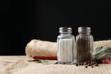 Ahşap masa üzerinde baharatlı tuzluk ve biber karıştırıcılar siyah arkaplan karşı, metin için boşluk