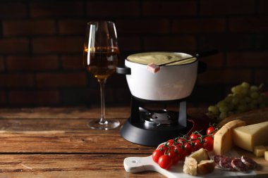Lezzetli eritilmiş peynirli fondü, ahşap masada atıştırmalıklar ve şarap.