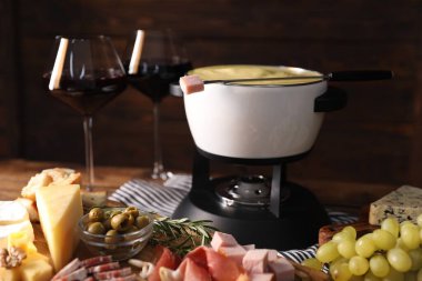 Lezzetli eritilmiş peynirli fondü, ahşap masada atıştırmalıklar ve şarap.