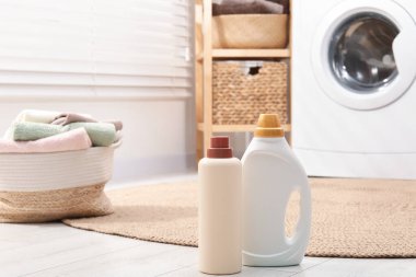 Deterjan şişeleri ve çamaşır sepetinin içinde havlular var.