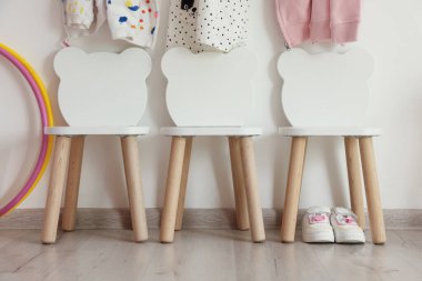 Oyun odasındaki ışıklı duvarda şık sandalyeler ve elbiseler asılı.