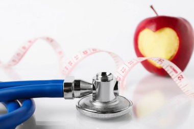Olgun elma, oyulmuş kalp, steteskop ve mezura beyaz masada, yakın plan.