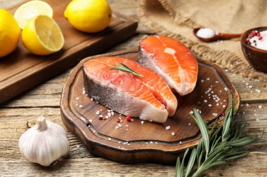 Taze somon filetosu, tuz, sarımsak, biberiye ve limon parçaları ahşap masada, yakın plan.