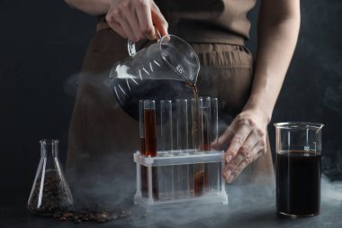 Siyah masada cam test tüpüne damlatan kadın, yakın plan.