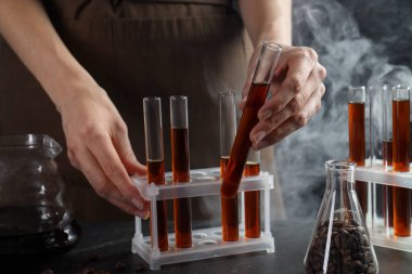 Elinde cam test tüpleri olan kadın kahve, fasulye ve sigara siyah masada, yakın plan.